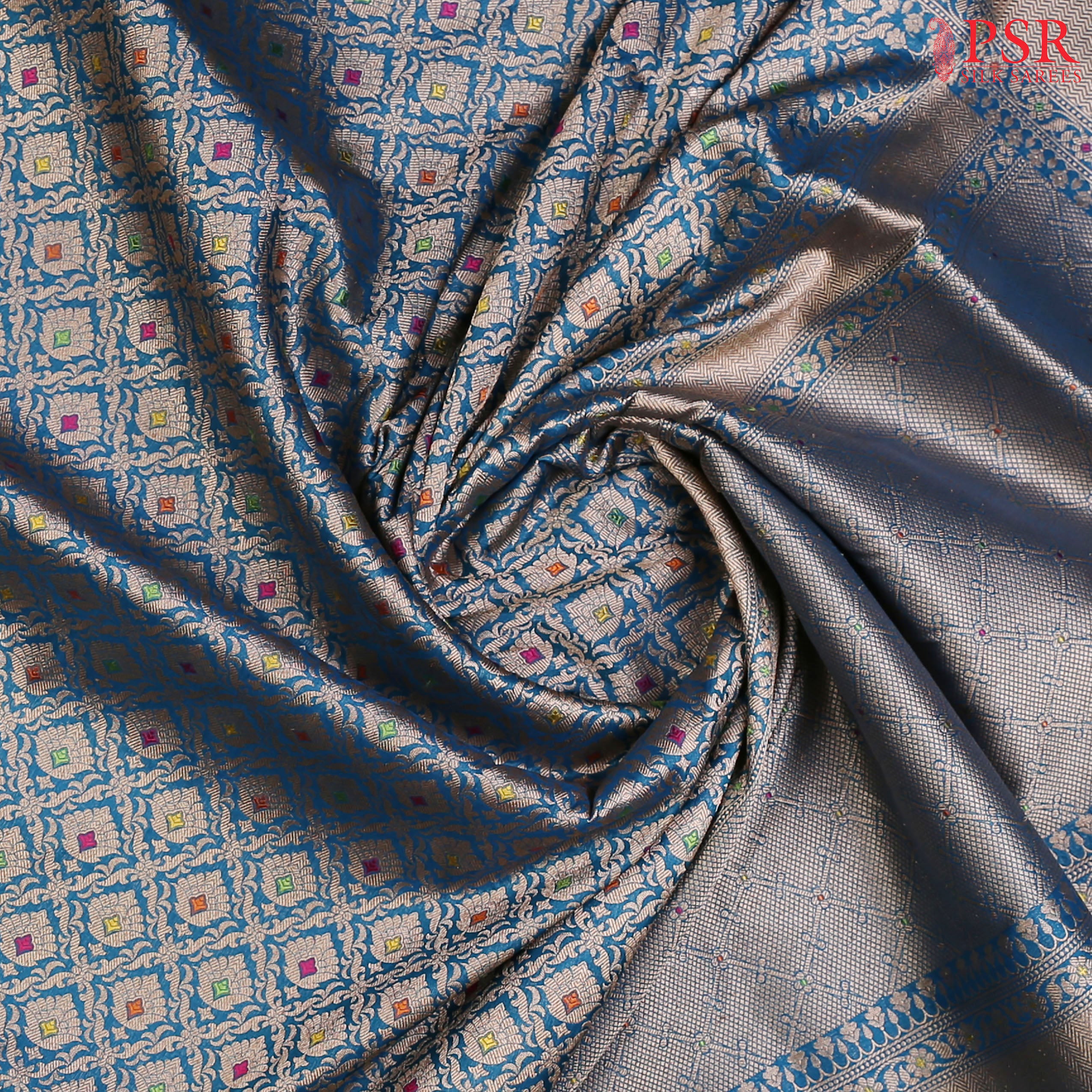 PSR Silks presents a stunning Peacock Blue Banarasi Silk Saree, showcasing a masterfully woven zari lattice pattern, beautifully embellished with vibrant thread work.