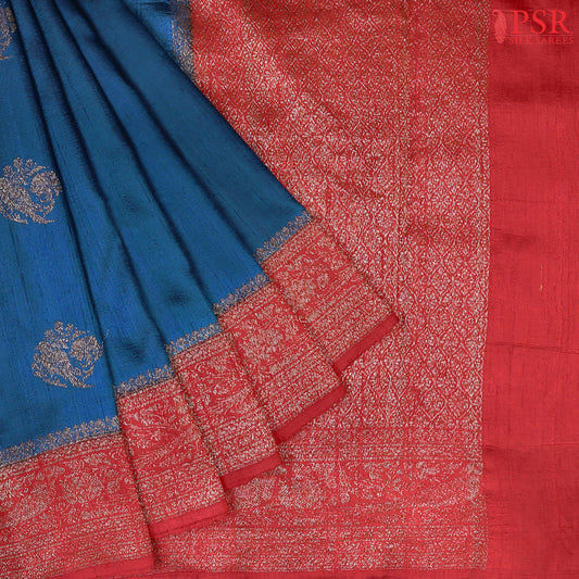 Unveil a world of elegance with this stunning Peacock Blue Banaras Jute Silk Saree, beautifully paired with a vibrant Red accent. 